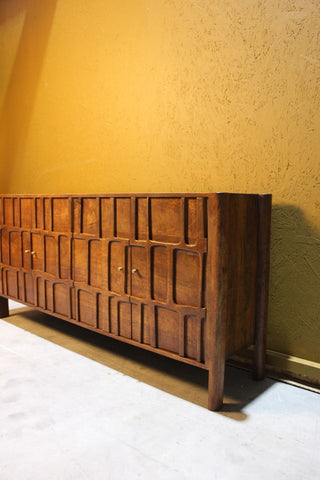 Sideboard with four carved wooden doors and brass handles against yellow wall