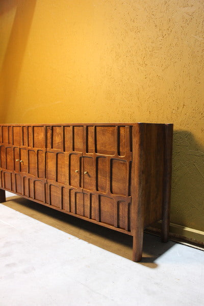 Sideboard with four carved wooden doors and brass handles against yellow wall