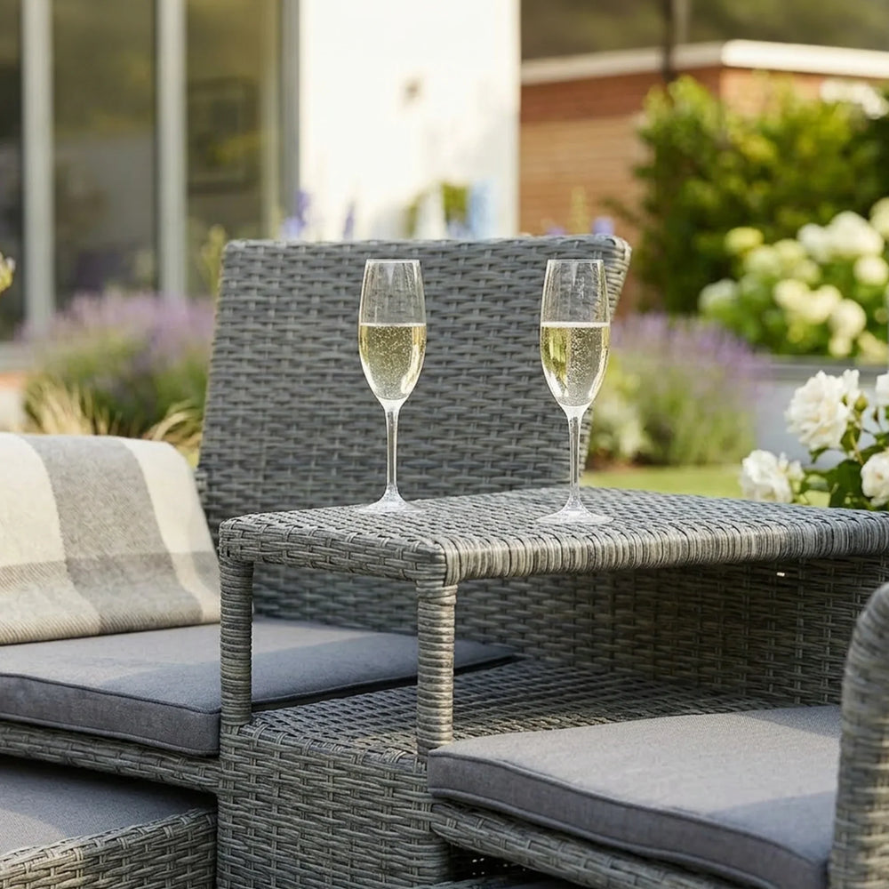 Grey rattan garden sofa set with glass table, two champagne flutes, and seat cushions