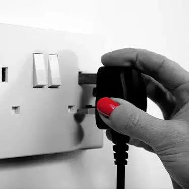 A hand plugging in an Atmos electric fire into a wall socket.