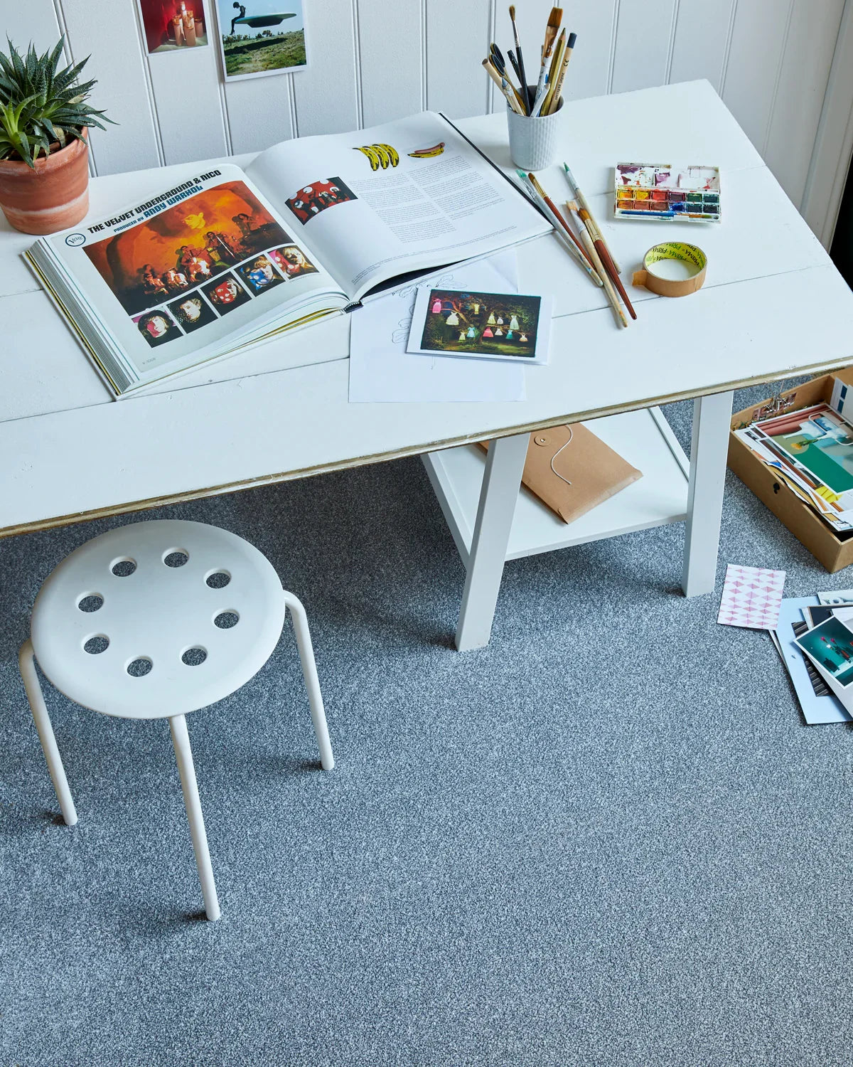 White desk with art supplies on soft grey carpet in creative studio setting