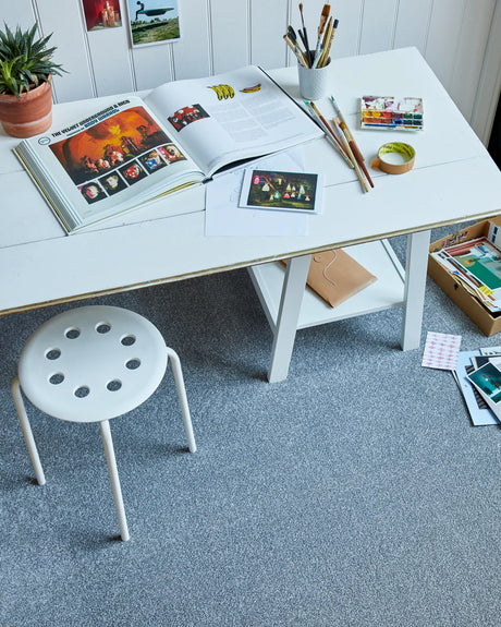 White desk with art supplies on soft grey carpet in creative studio setting