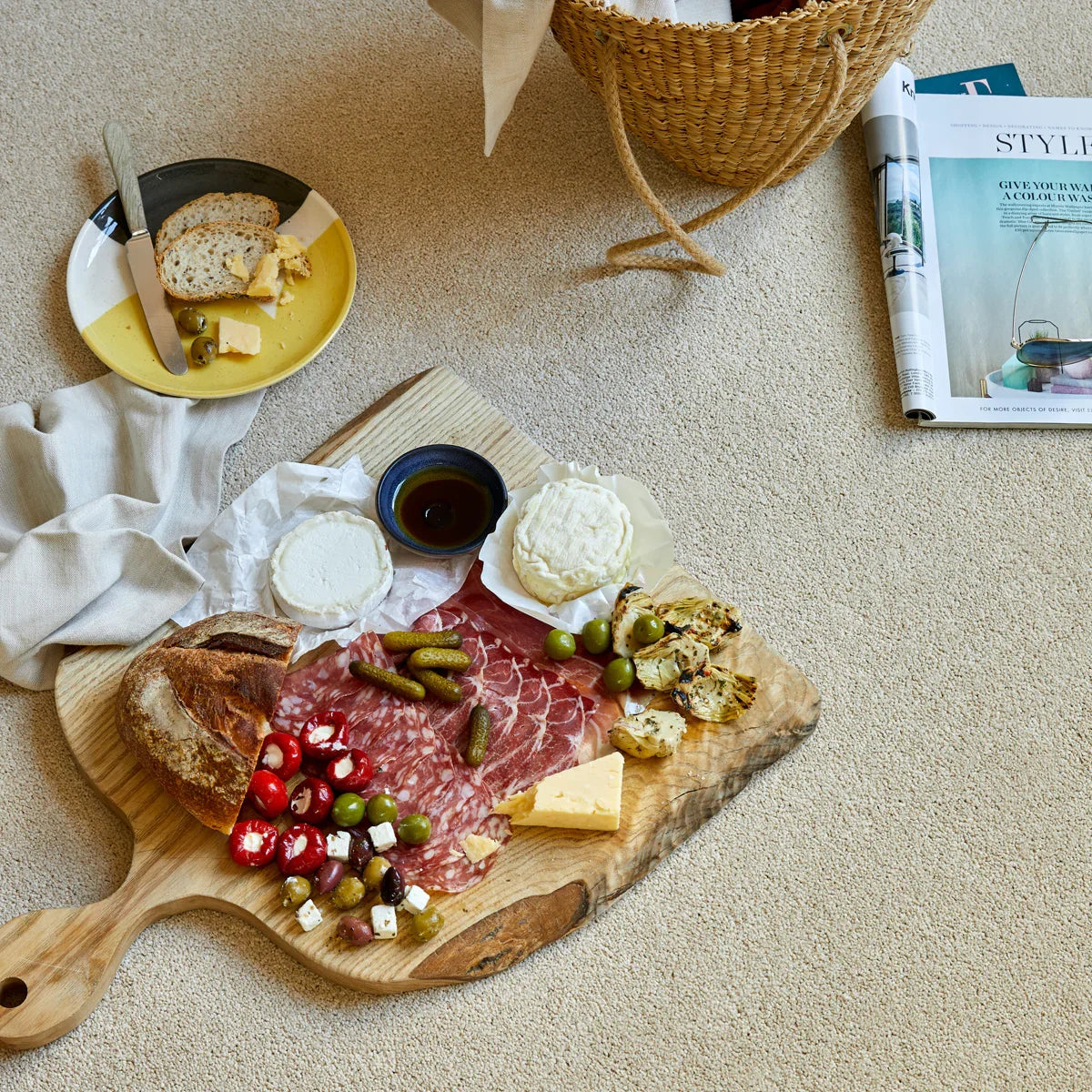Wooden serving board with assorted cheeses, cured meats, and olives on a beige carpet.