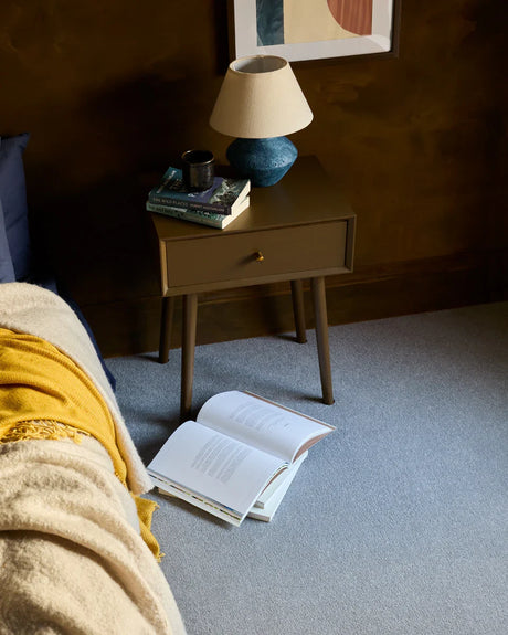 Brown wooden bedside table with books and a blue lamp, styled in a cozy bedroom scene.