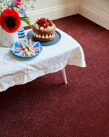 Rich burgundy carpet in dining area with cake on white tablecloth and floral decor