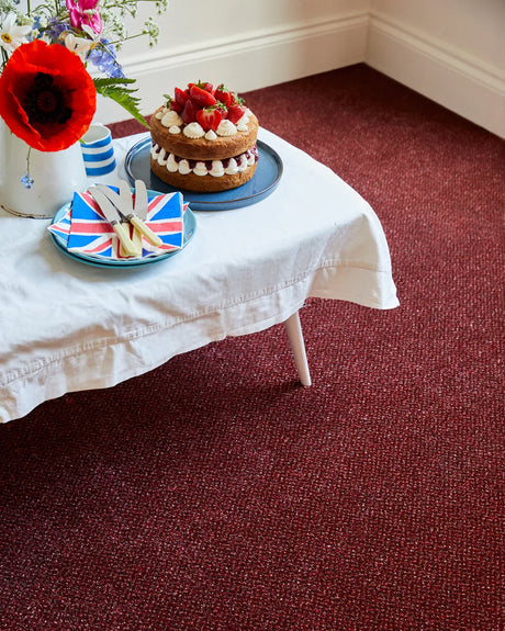 Rich burgundy carpet in dining area with cake on white tablecloth and floral decor