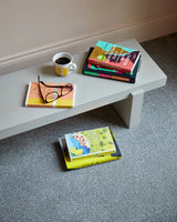 Light grey wooden bench with books and a mug on textured grey carpet