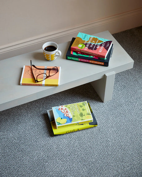 Light grey wooden bench with books and a mug on textured grey carpet