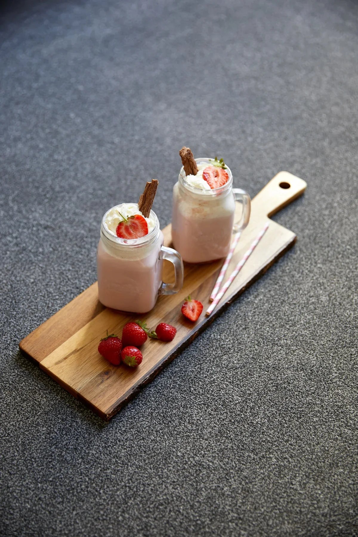 Grey carpet with two strawberry milkshakes on a wooden board, garnished with strawberries.