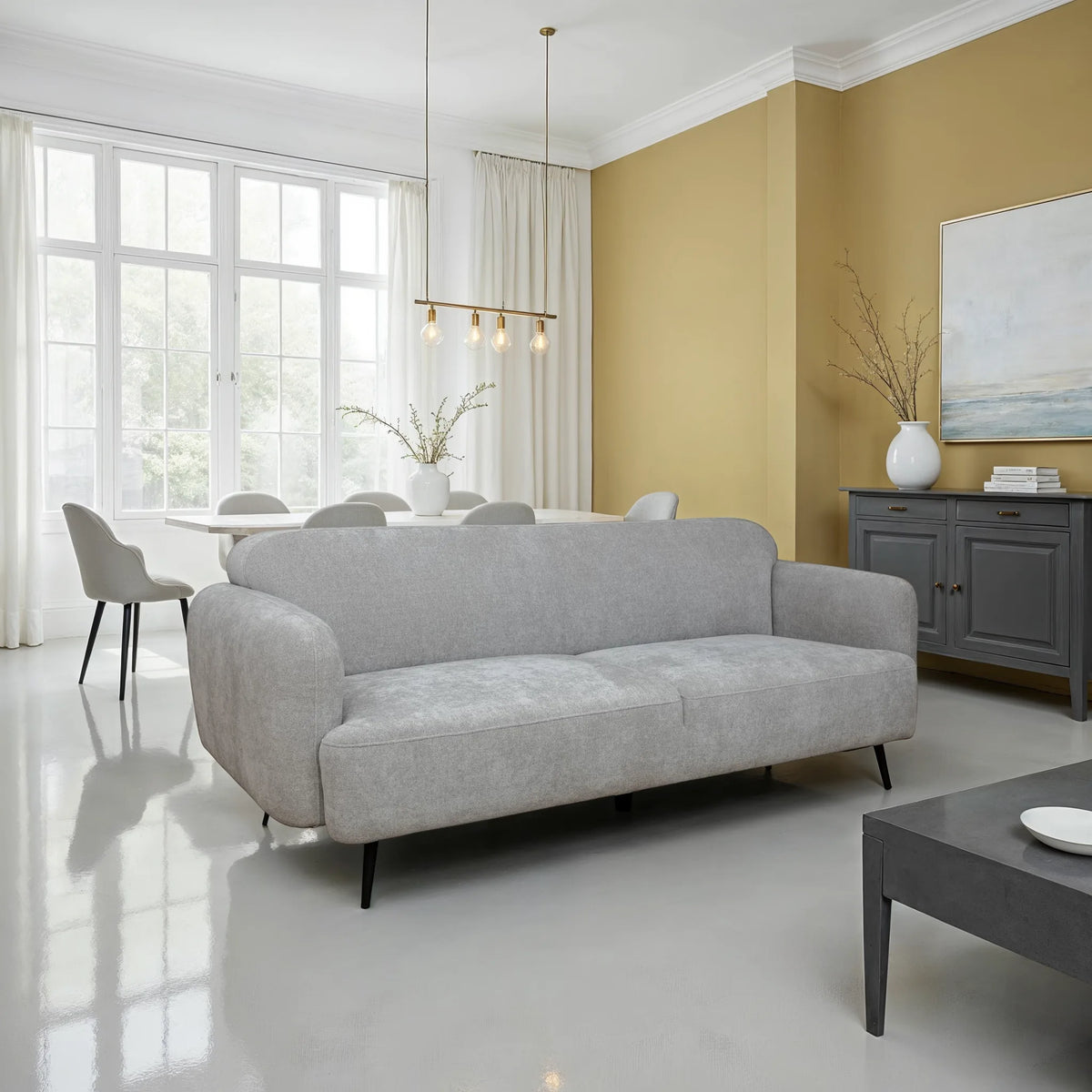 Light gray upholstered sofa with rounded arms and slim black legs styled in a modern living room with a warm beige accent wall, large windows, pendant lighting, and contemporary decor.