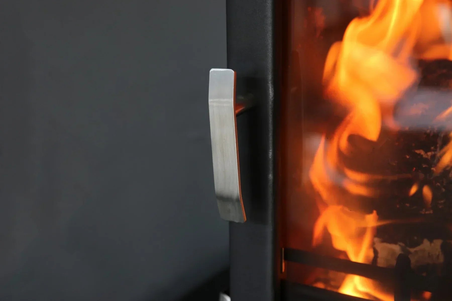 Brushed metal stove door handle on black 8kW wood burner with visible fire inside