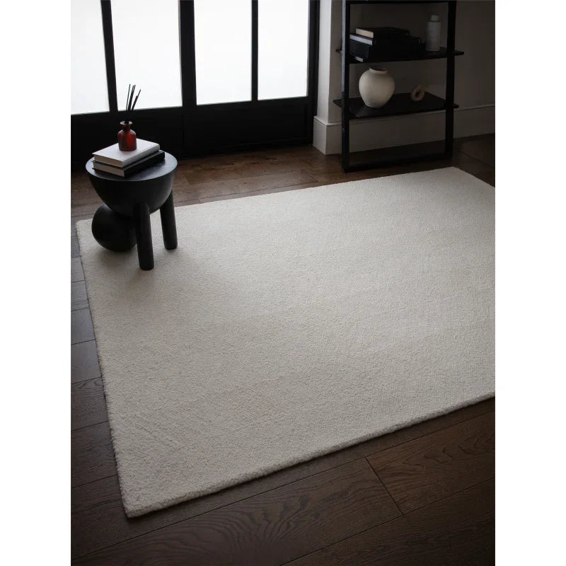 Cream area rug on dark wood floor beside modern black side table and shelving
