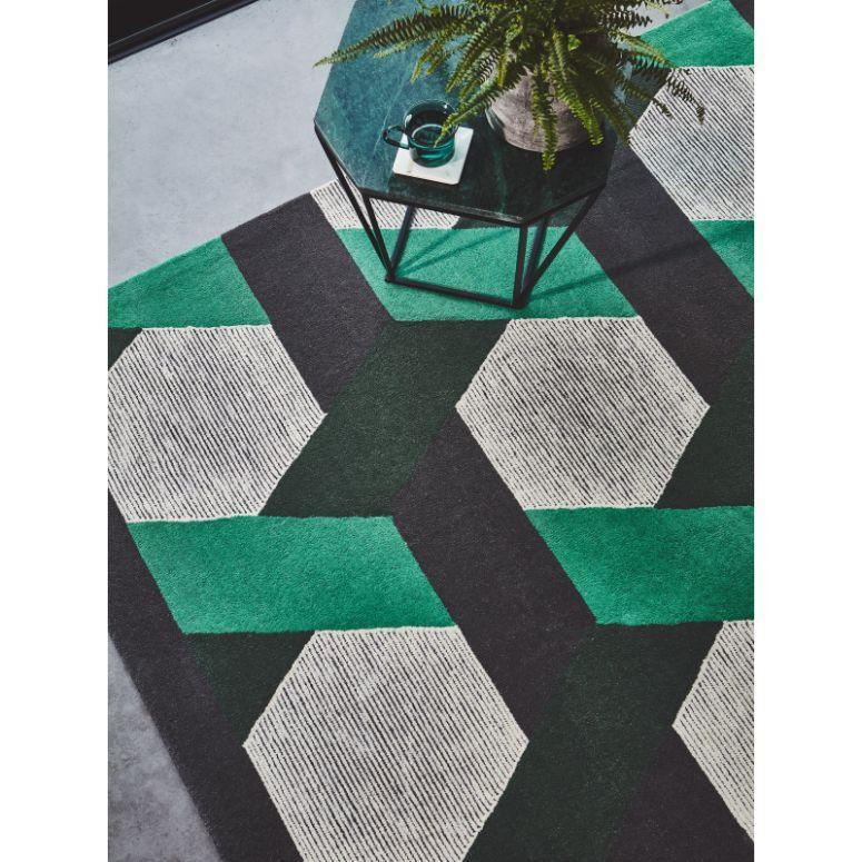 Geometric area rug in green, black, and cream with glass coffee table and plant