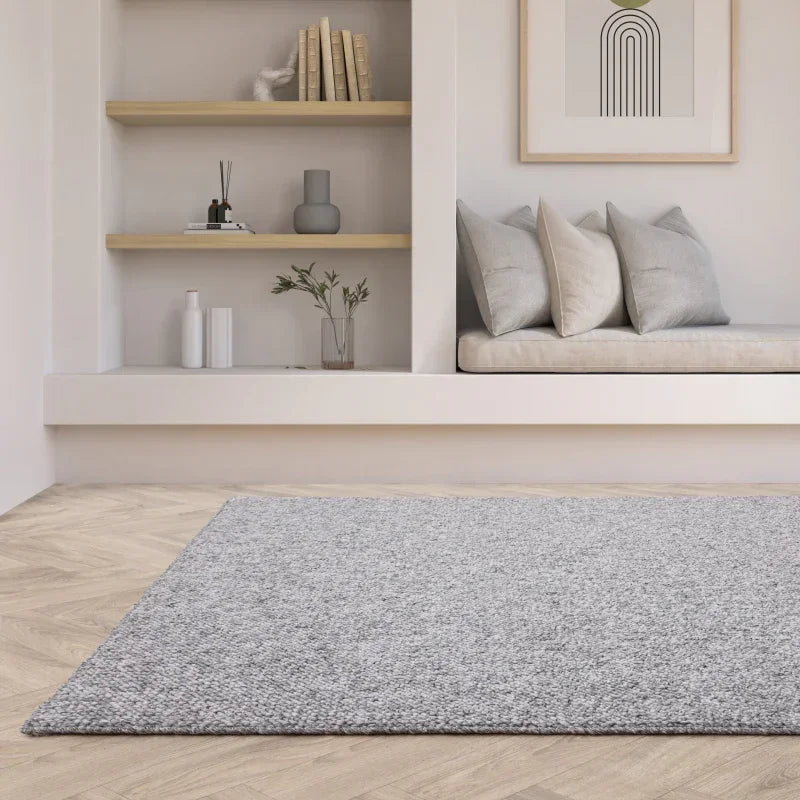 Grey textured area rug on herringbone wood floor in modern living room with built-in shelves
