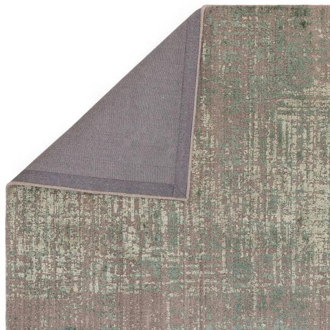 Green and beige patterned area rug with corner folded to show backing