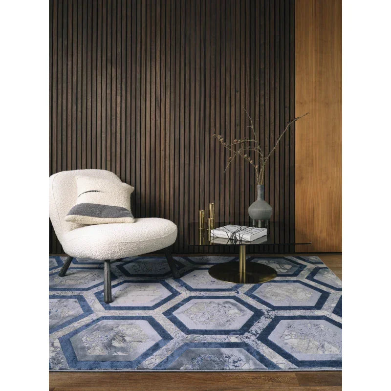Blue geometric patterned rug under modern cream armchair with cushion and glass side table