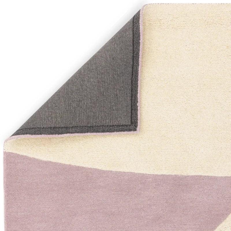 Pastel area rug with cream and mauve geometric design, corner flipped to show backing