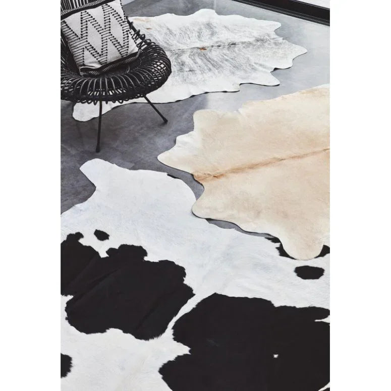 Cowhide rugs in black and white, beige, and grey on concrete floor with rattan chair