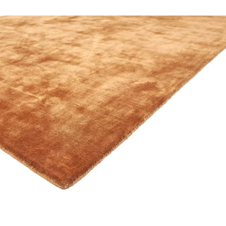 Corner view of a rectangular rust orange velvet rug with a soft textured finish