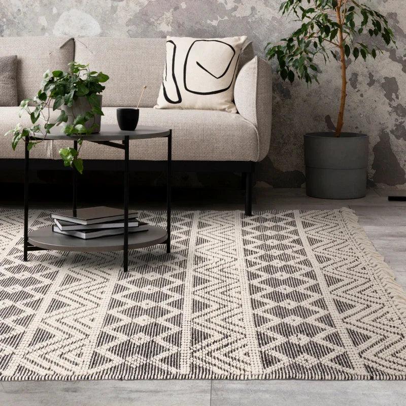 Geometric patterned rug under modern beige sofa with abstract cushion and round black table