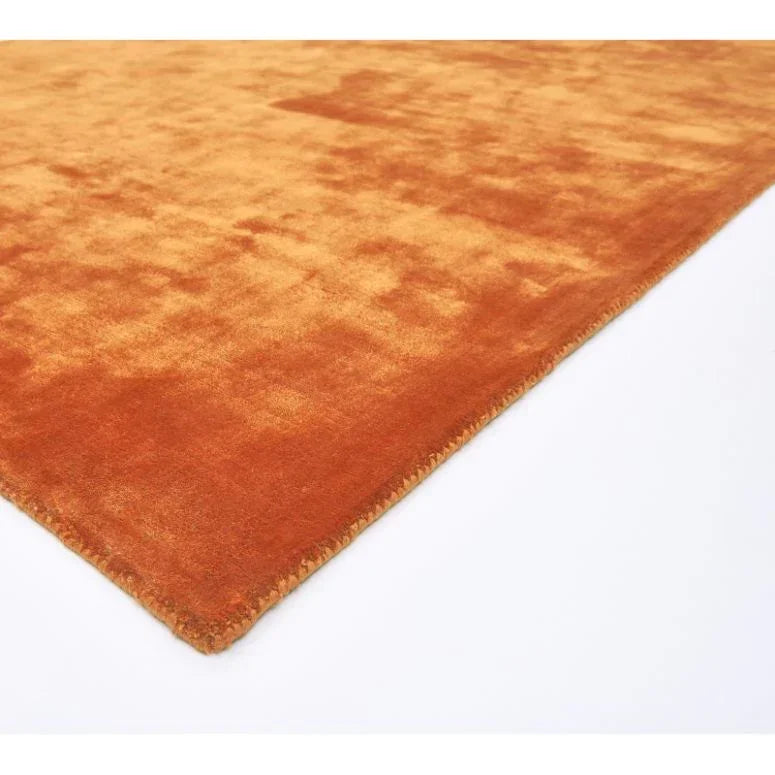 Closeup of rectangular orange area rug with soft textured pile on white background