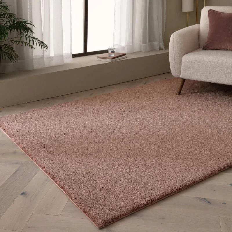 Blush pink area rug on light wood floor beside cream sofa in modern living room