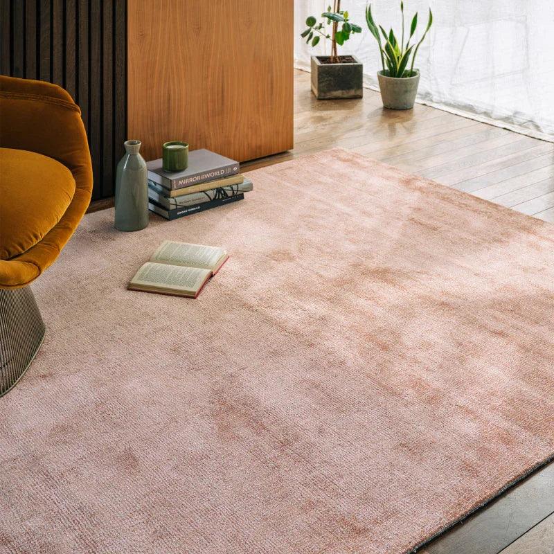 Light pink area rug in modern living room with mustard chair, books, and potted plants