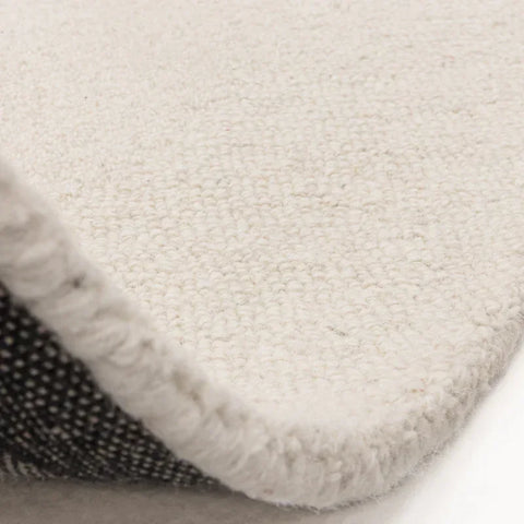 Close-up of cream wool rug corner showing textured loop pile and woven backing
