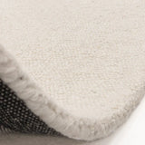 Close-up of cream wool rug corner showing textured loop pile and woven backing