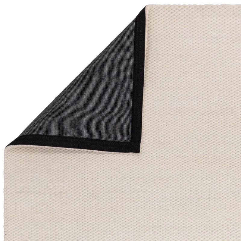 Closeup of cream textured rug with black lined corner folded over