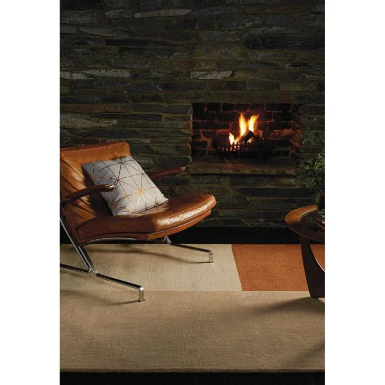 Modern brown leather armchair and geometric rug in living room with stone fireplace