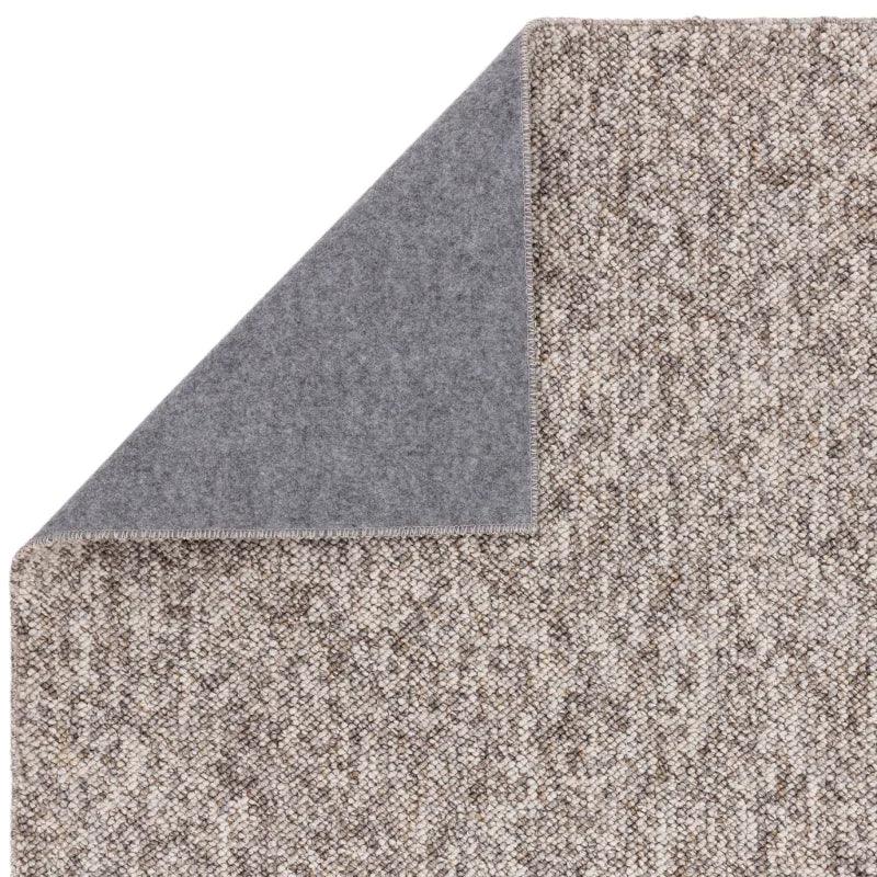 Beige woven rug with a grey felt non-slip backing, corner folded to show underside