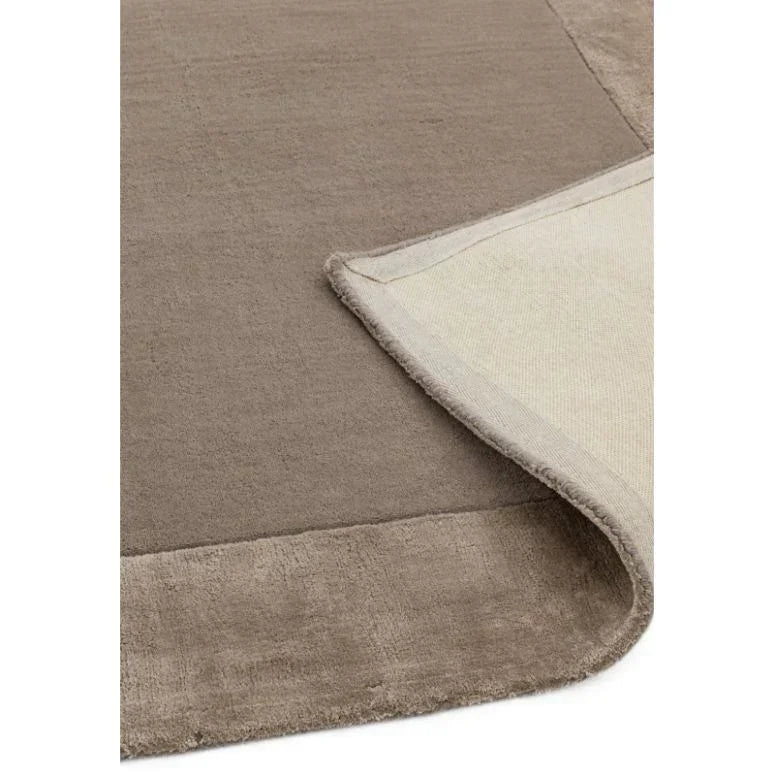 Taupe area rug with soft texture and visible border detail, one corner folded up