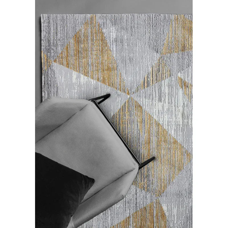 Geometric area rug with gold and grey pattern under grey armchair and black cushion