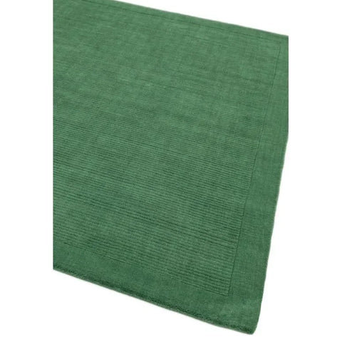 Green area rug with subtle textured pattern and solid border, close-up corner view