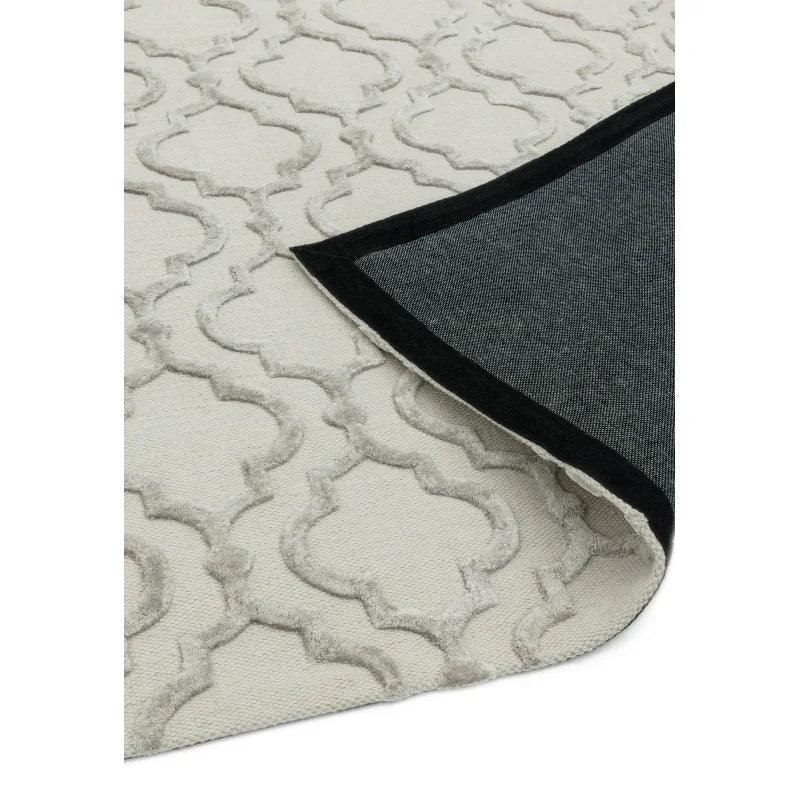 Cream patterned rug with textured geometric design, corner folded to show black trimmed backing
