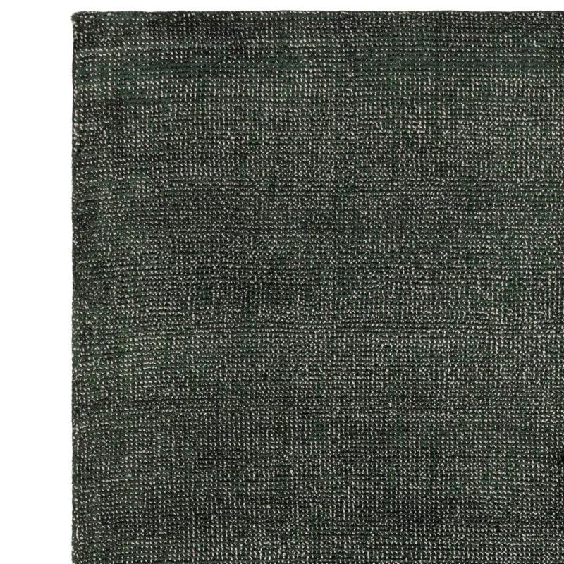 Closeup of dark green textured rug fabric corner with woven detailing