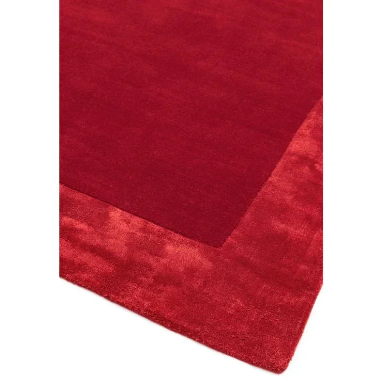 Red area rug with a solid center and plush textured border, corner view