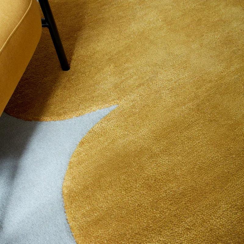 Mustard yellow area rug with abstract shape next to sofa leg on light floor