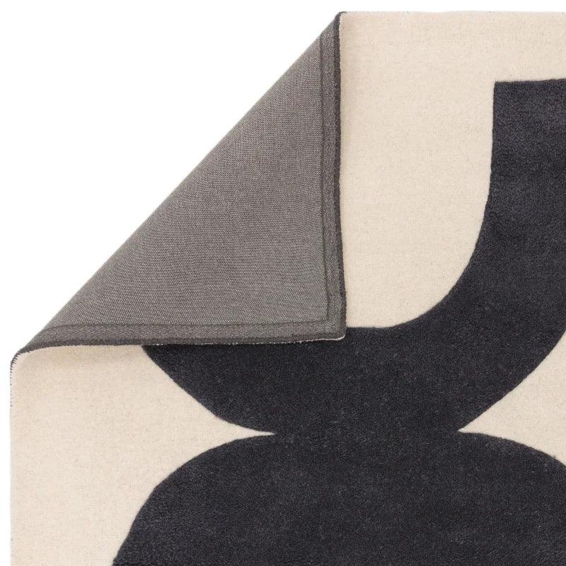 Closeup of modern area rug with bold black pattern and corner folded to show backing