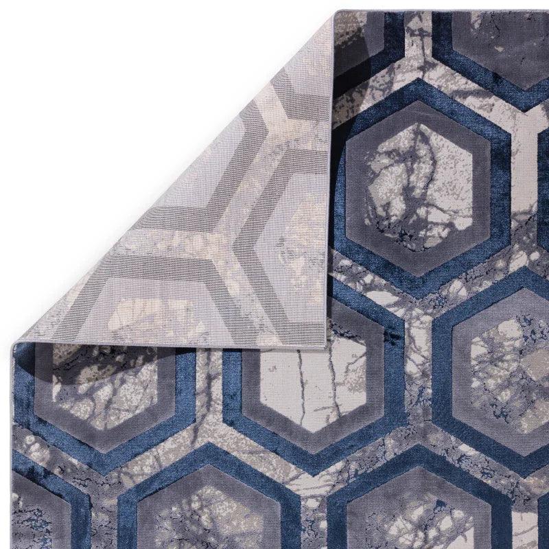 Geometric patterned area rug in blue and grey with corner folded to show backing