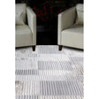 Modern striped area rug in grey and cream tones placed between two beige armchairs