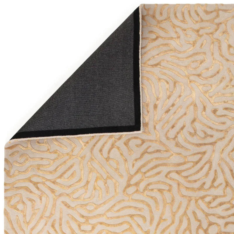 Beige and gold patterned area rug with black fabric backing, close-up corner view
