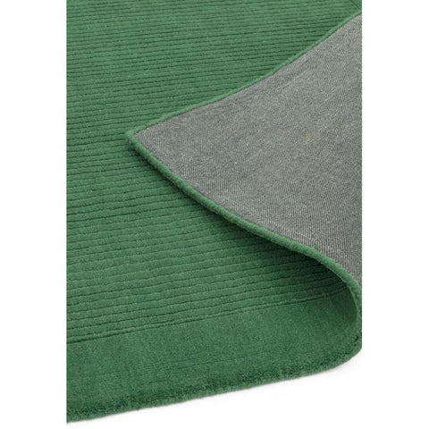 Green ribbed area rug with corner flipped to show grey fabric backing