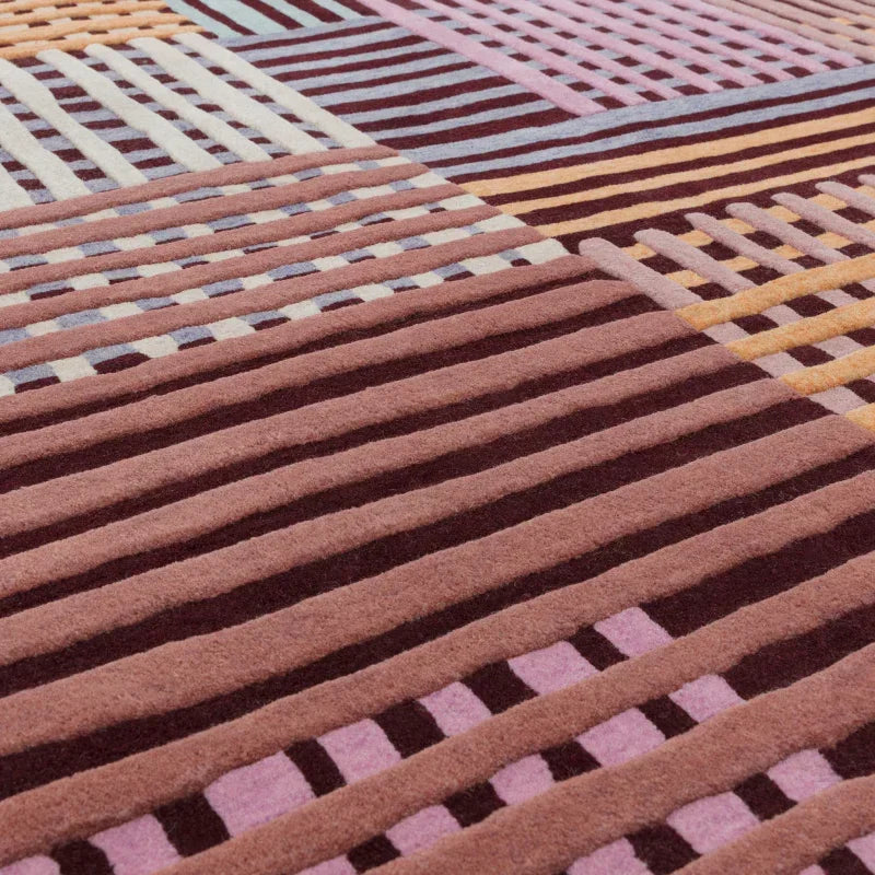 Geometric wool rug with pink, burgundy, cream, and yellow linear patterns, close up view