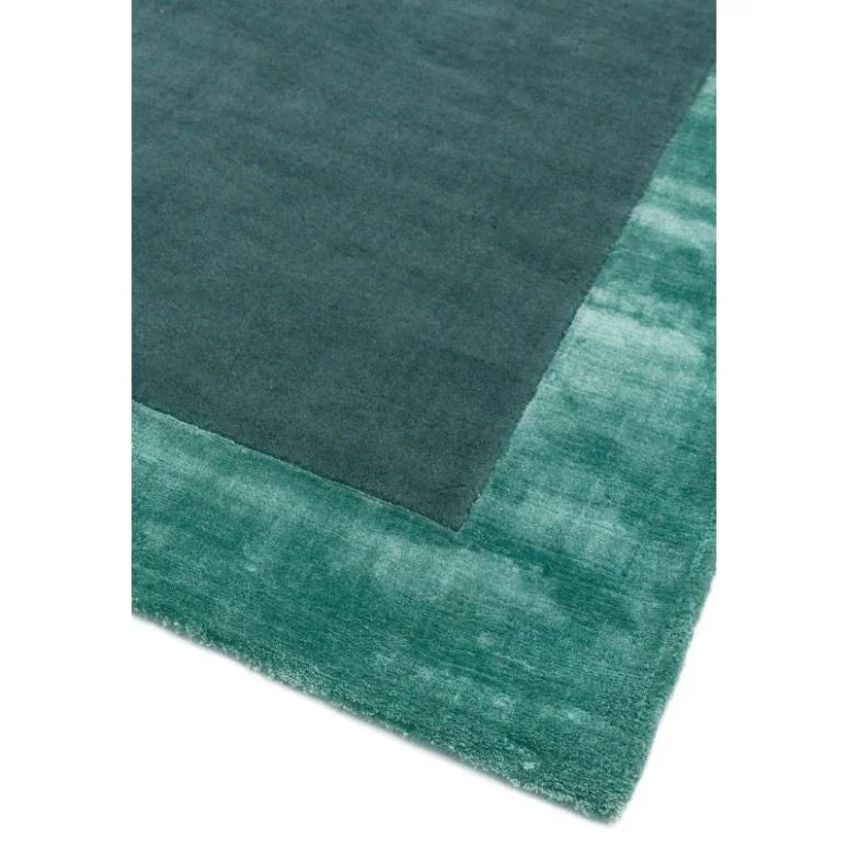 Green bordered area rug with plush pile and two-tone color design, close-up corner view