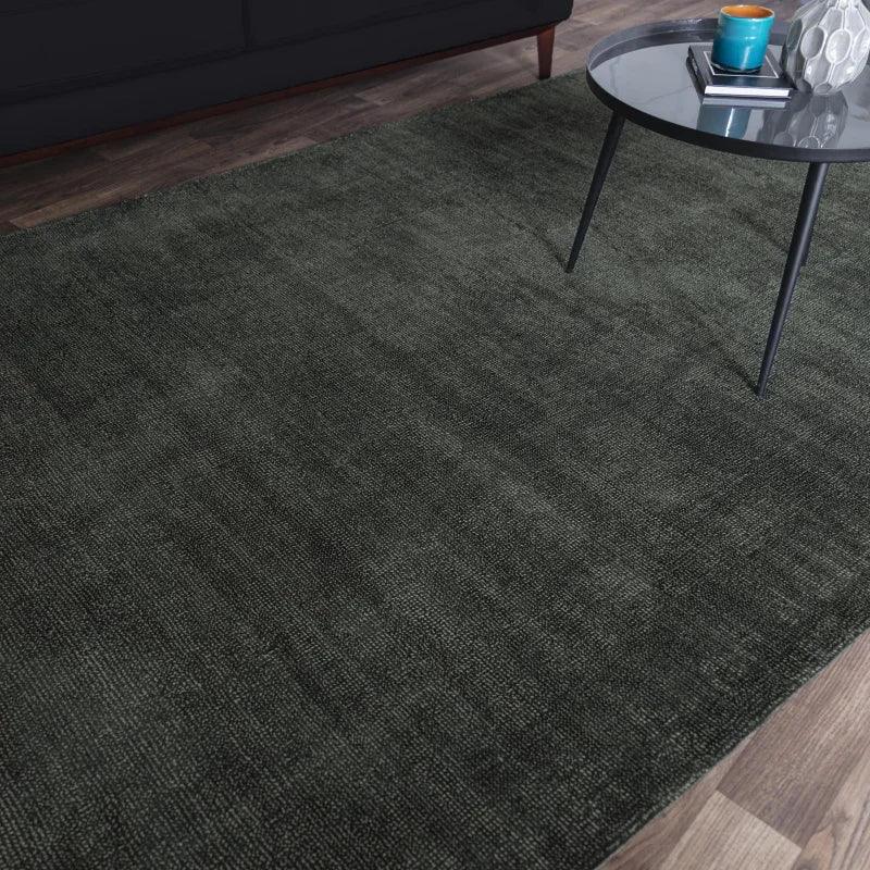 Dark grey area rug on wooden floor beside round coffee table and sofa