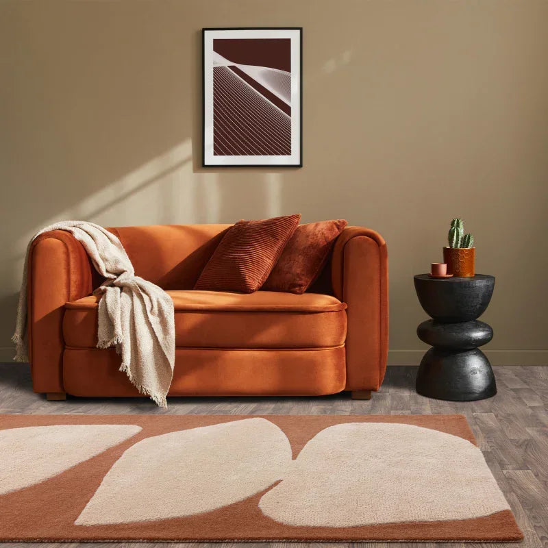 Orange velvet sofa with cushions and throw in living room, modern rug and black side table