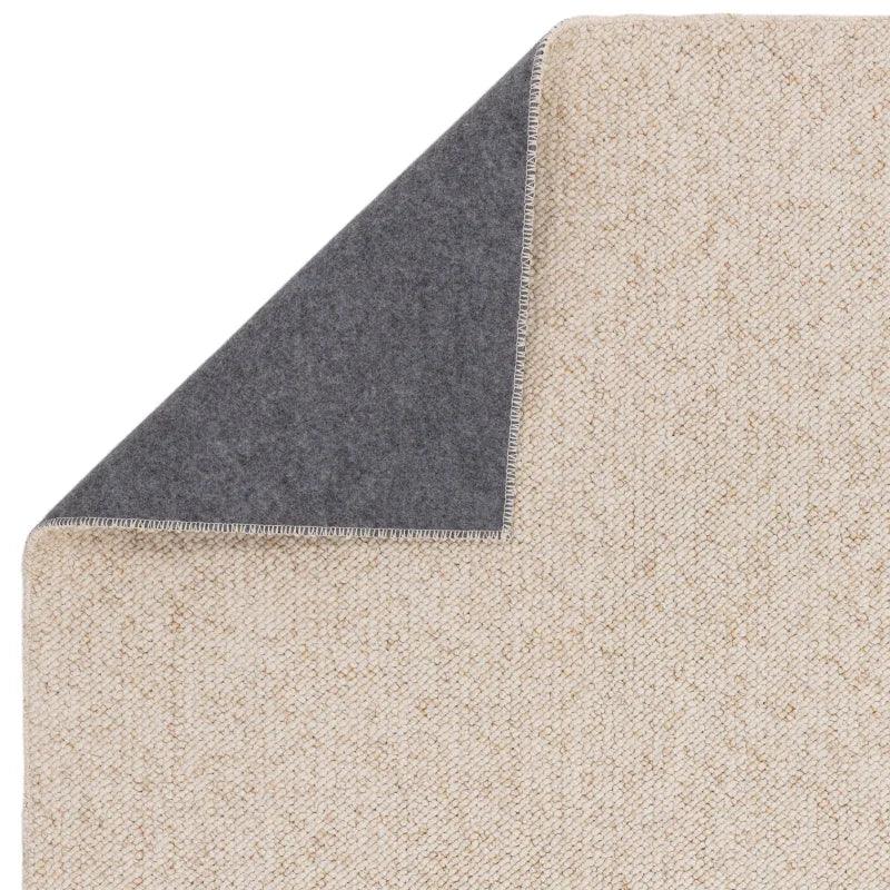Beige textured rug with grey felt backing, close-up on corner and stitching detail