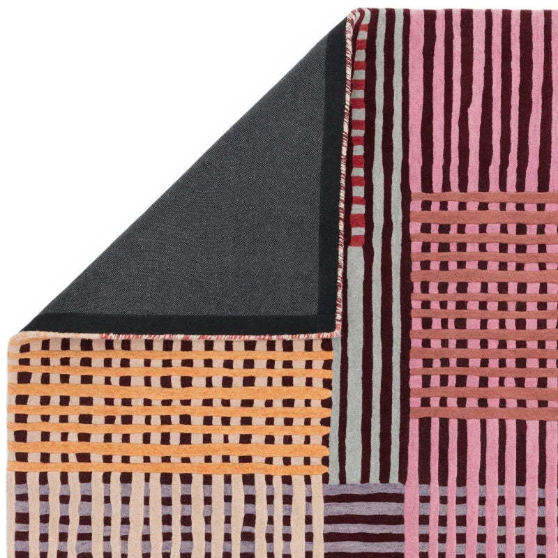 Geometric patterned rug with pink, yellow, and burgundy lines and folded corner detail